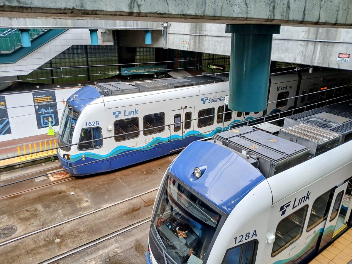 A light rail train on elevated tracks in Seattle, with the city's downtown buildings visible.