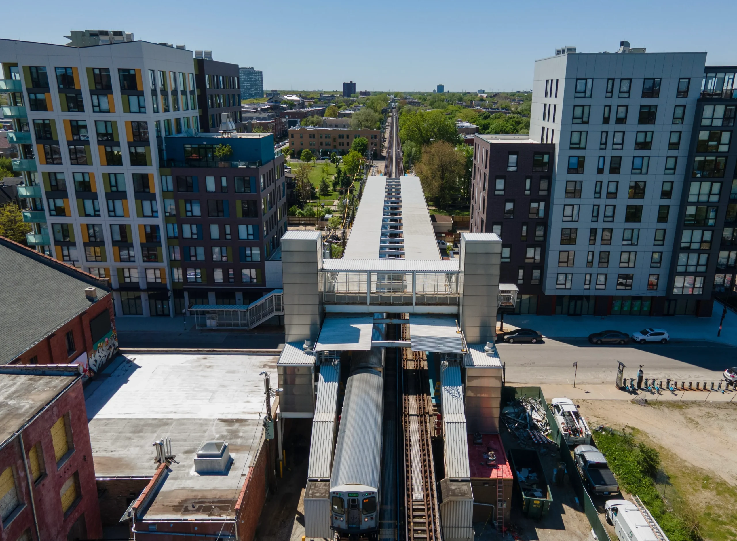 A modern apartment building with ground-floor retail, situated adjacent to an elevated train station in Chicago, illustrating a transit-oriented development.