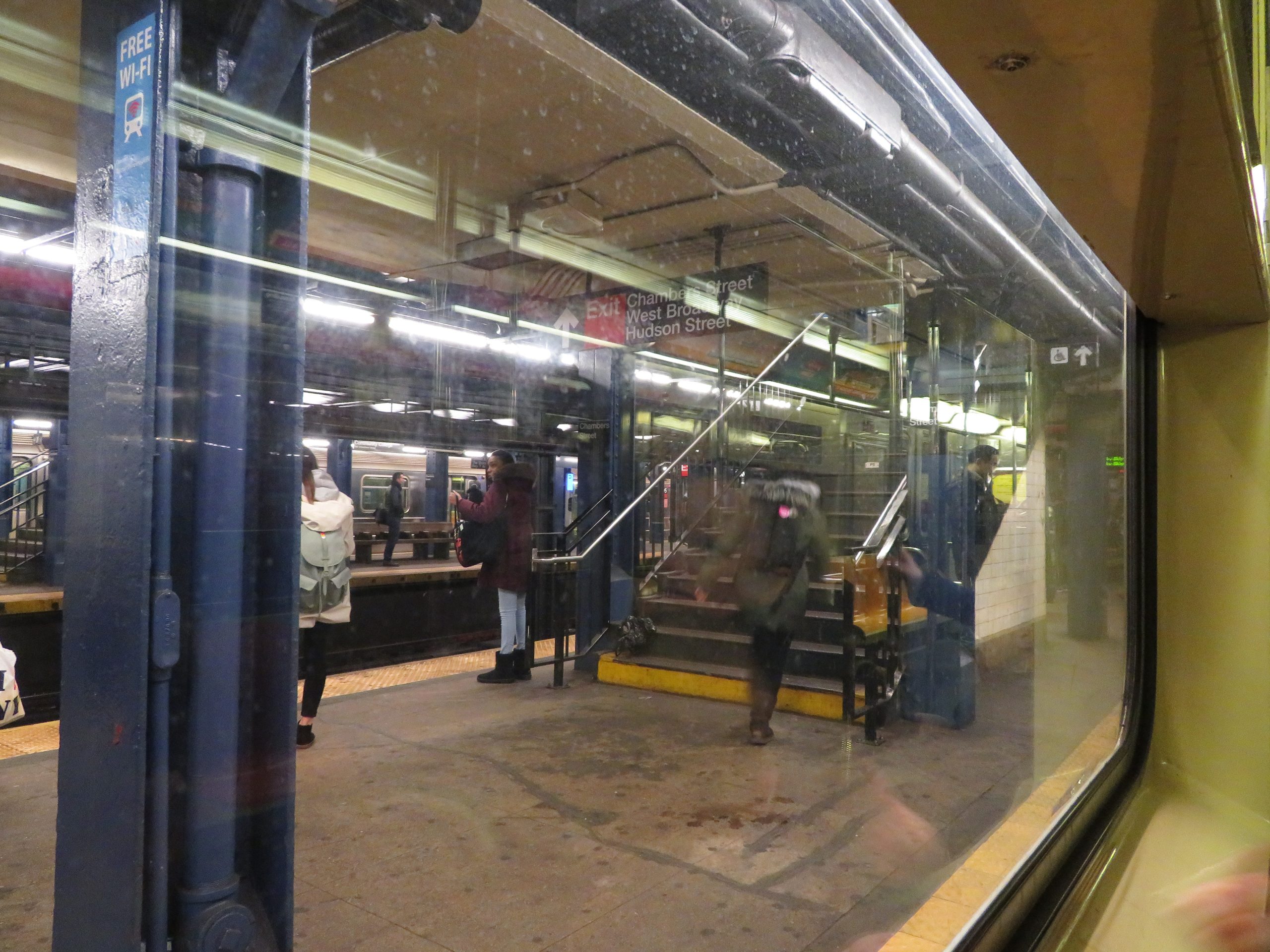 A modern subway train arriving at a station platform in New York City, with digital signage visible.