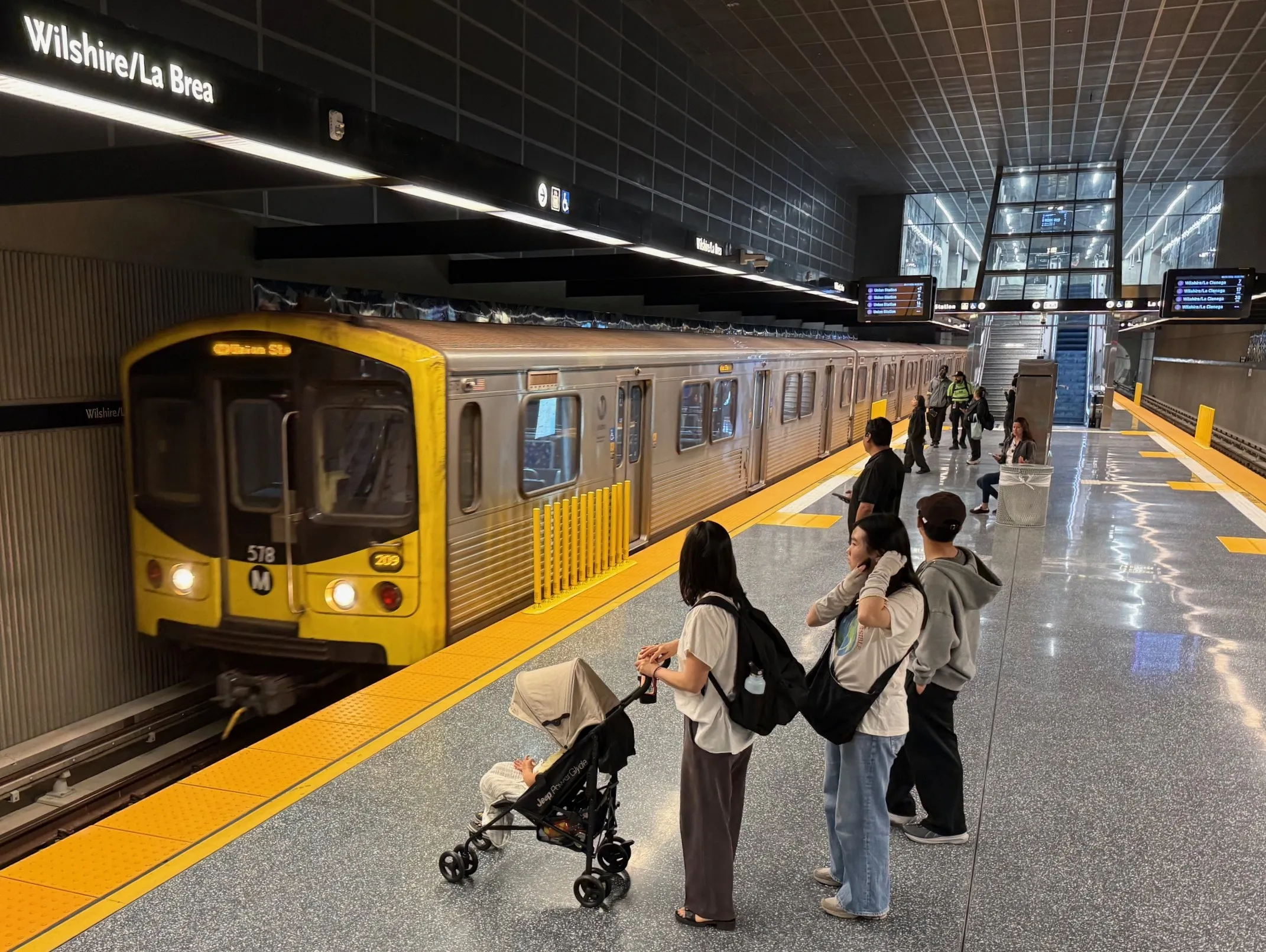 A modern Los Angeles D Line subway station interior with passengers waiting on the platform.