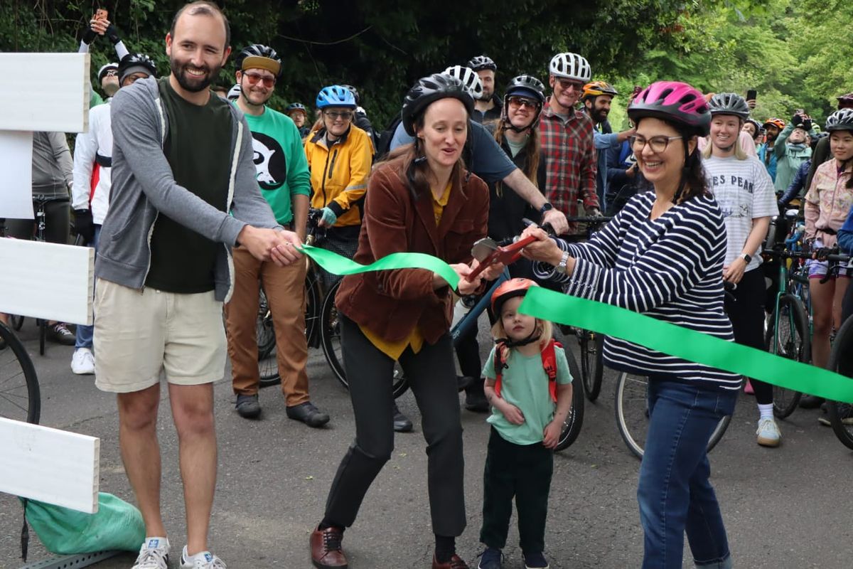 People cycling, walking, and rolling along a closed-off Lake Washington Boulevard in Seattle, with trees and water visible.