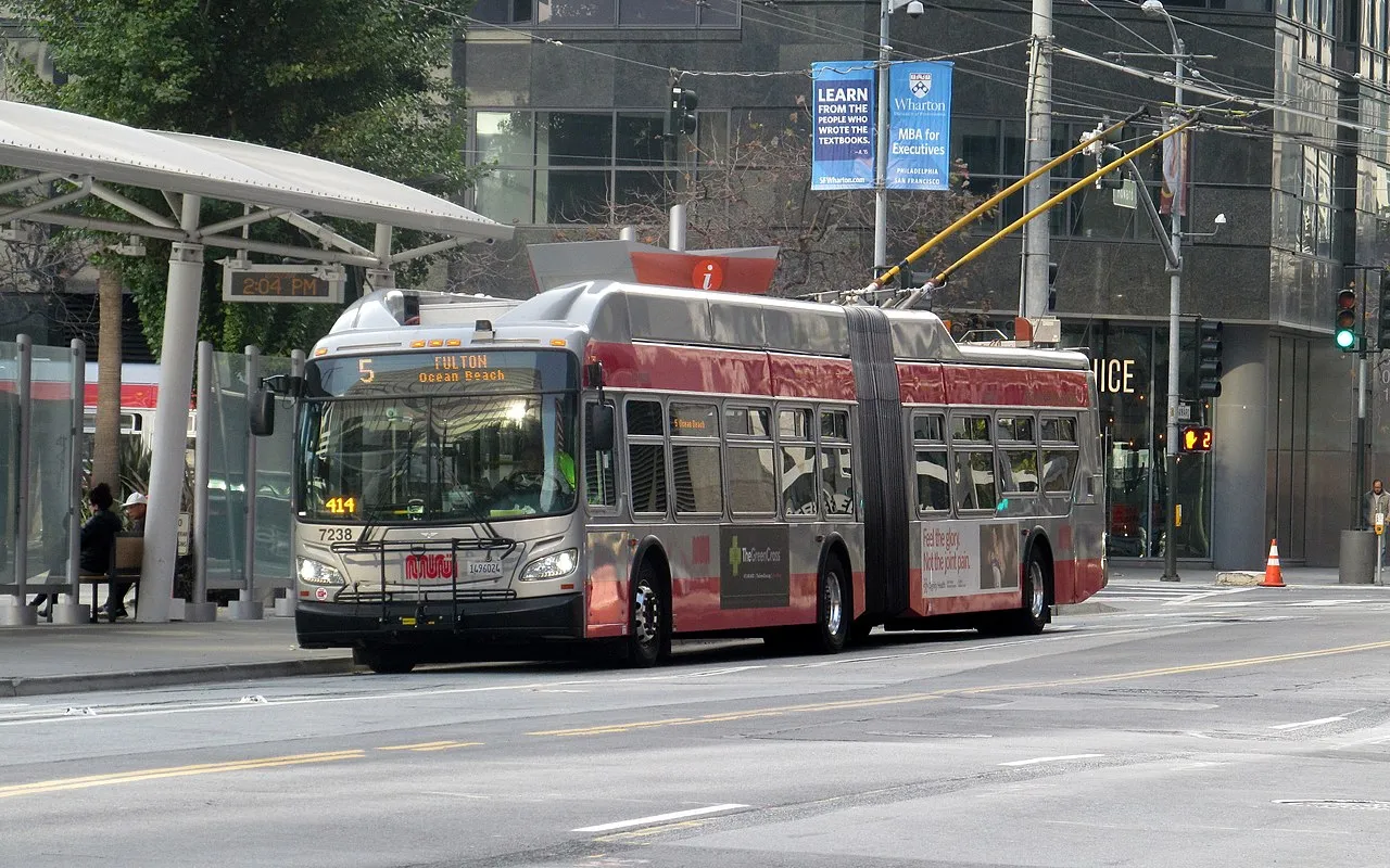 San Francisco Municipal Railway vehicles including a bus and a light rail train at a transit station.