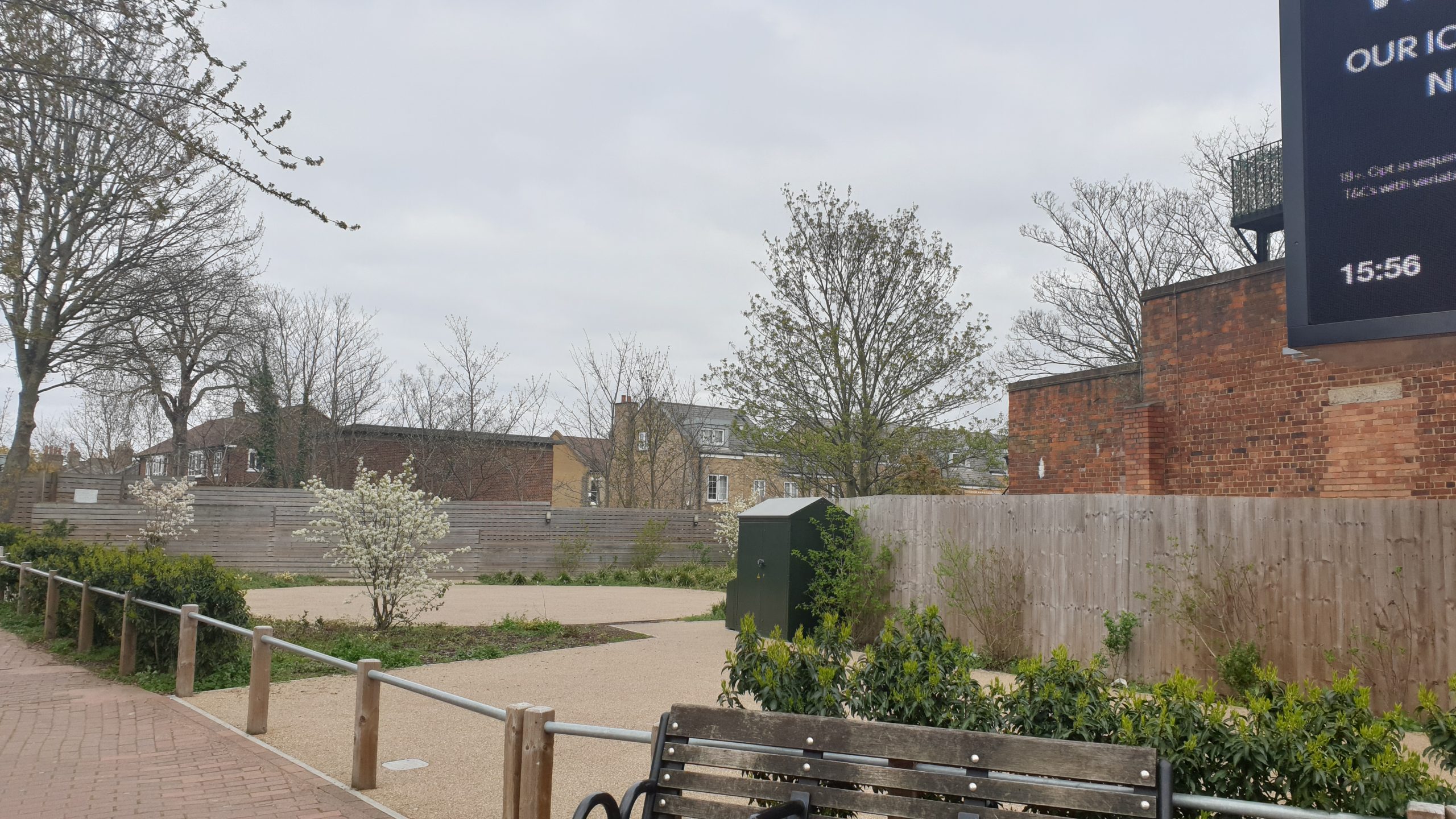 A small, vibrant pocket park nestled between tall buildings in London, with people enjoying the green space.