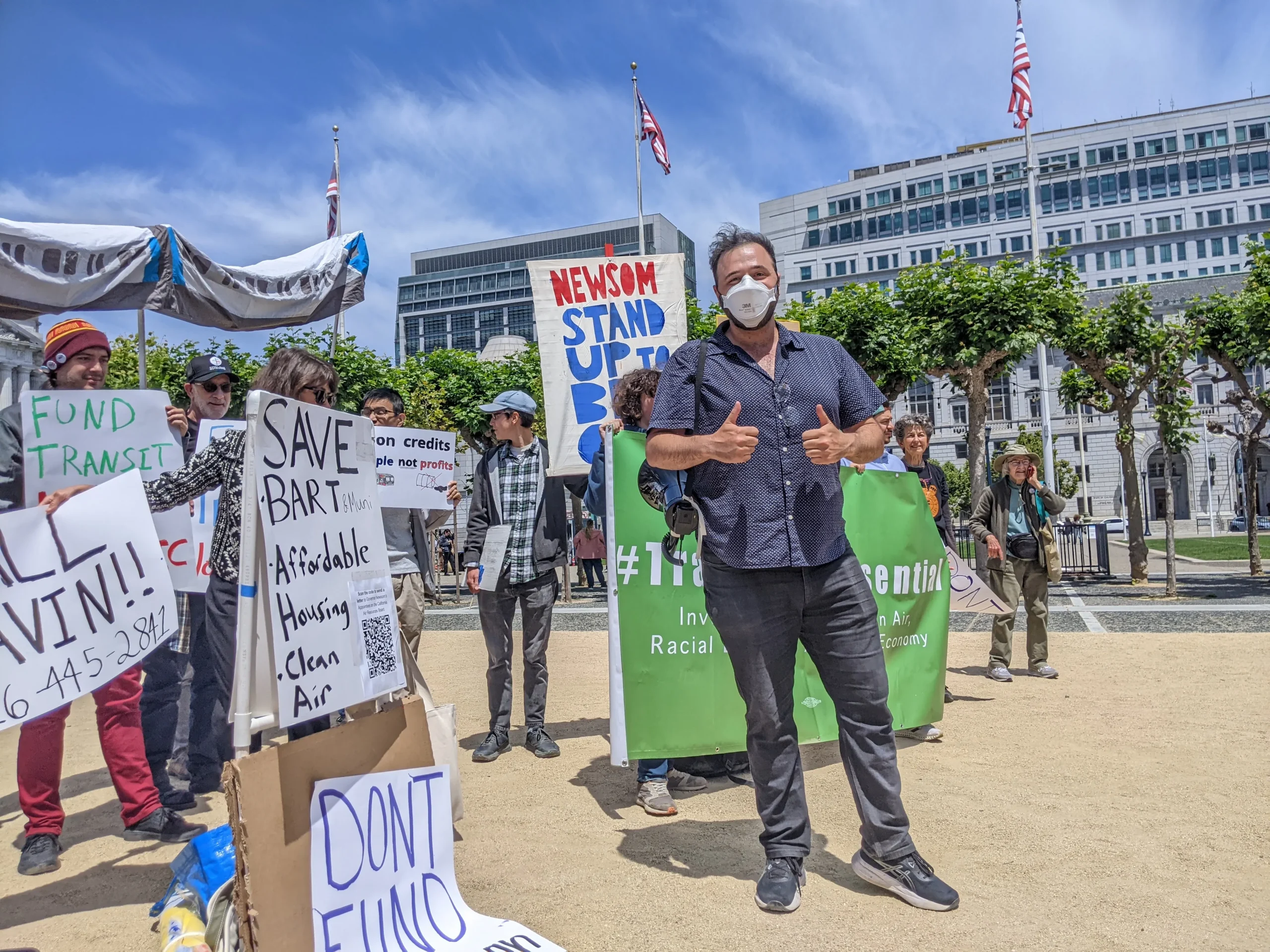 A diverse group of transit and environmental advocates holding signs and banners outside a government building in San Francisco.