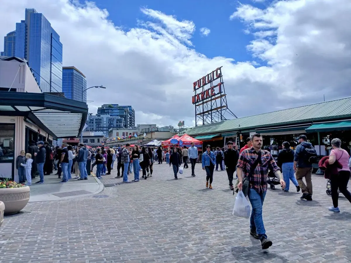 Pedestrians and vendors interacting in a vibrant Pike Place Market with temporary street closures and barriers in place.