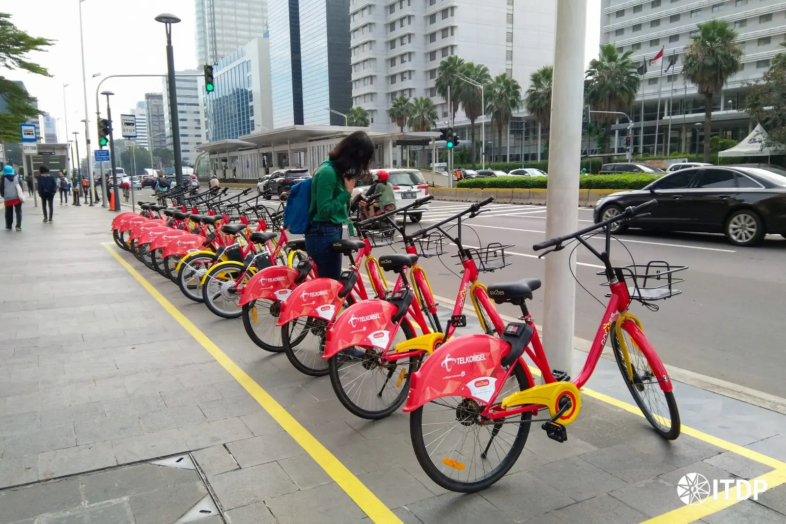 Jakarta bike-share station near MRT entrance, with commuters on bicycles and pedestrians, illustrating first‑mile connectivity