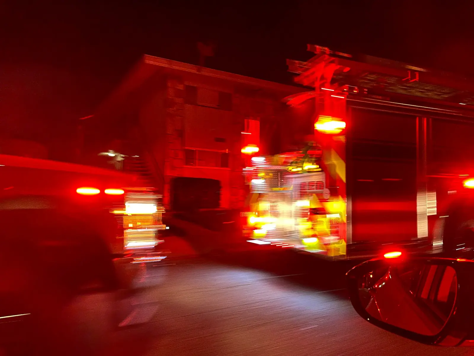An emergency vehicle with its lights flashing navigates a street, with a self-driving car in the vicinity.