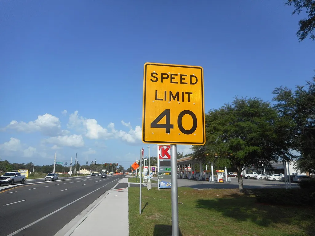 A London street sign indicating a speed limit, with traffic visible in the background.