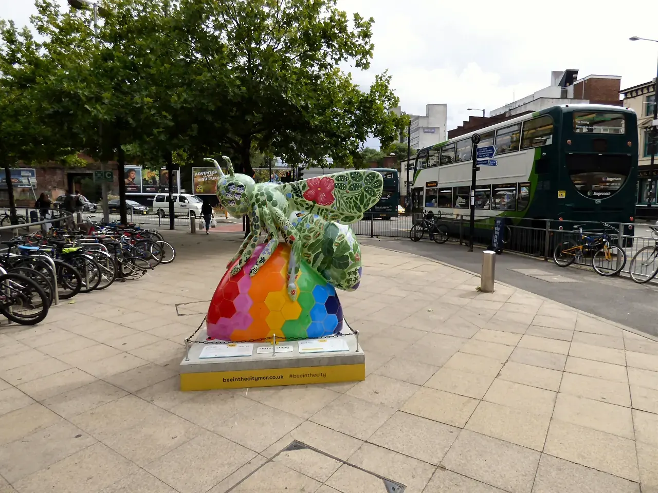 A diverse group of people walking through a London street, some pausing to observe public art installations, conveying a sense of engagement with the urban environment.