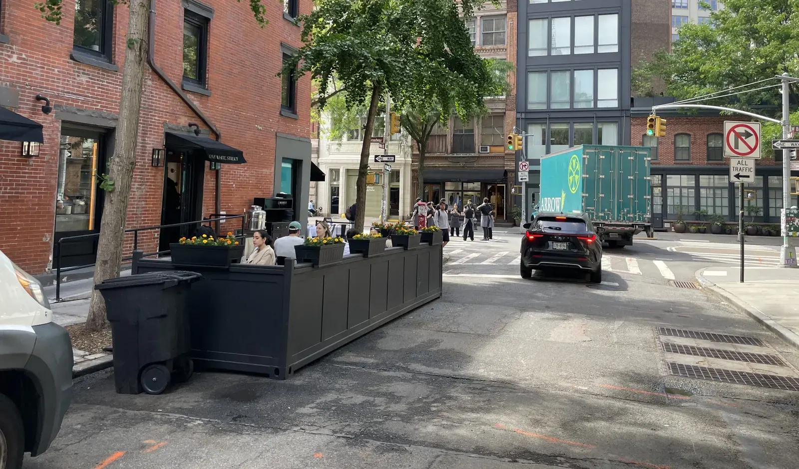 Outdoor dining tables set up on a New York City sidewalk with a protected bike lane and traffic in the background
