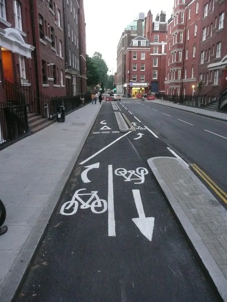 A speed camera mounted on a pole beside a London red route with a bus lane and cycle lane markings