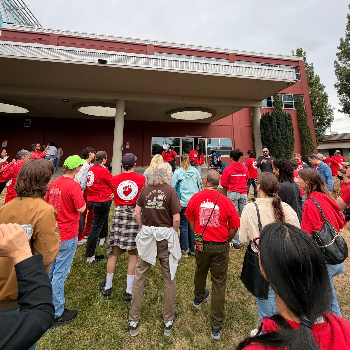 Seattle teachers on picket line outside a public school building, holding placards about class sizes and special education funding, with city skyline in background