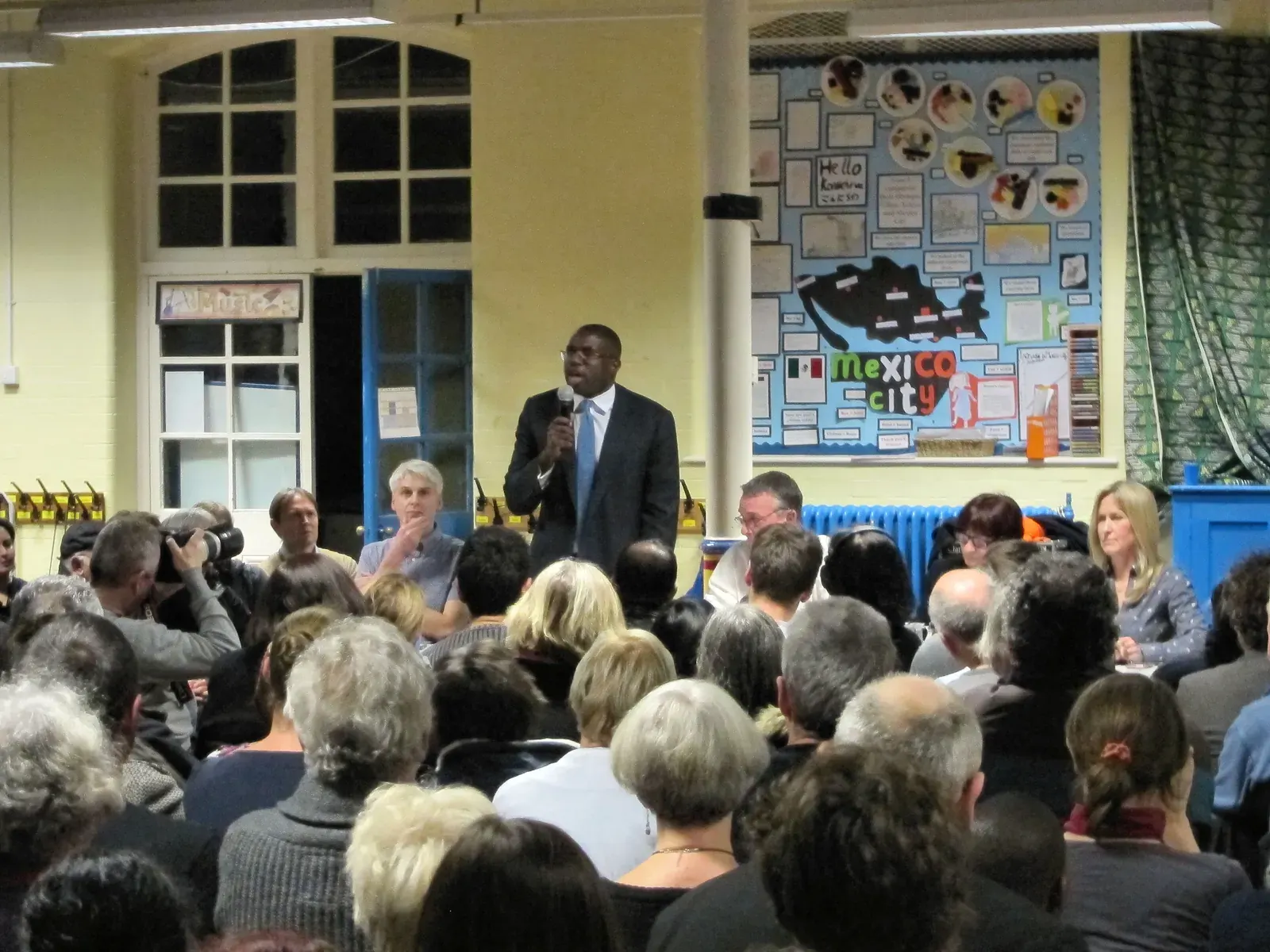 Residents at a public planning consultation in a London community hall, reviewing large site plans and maps
